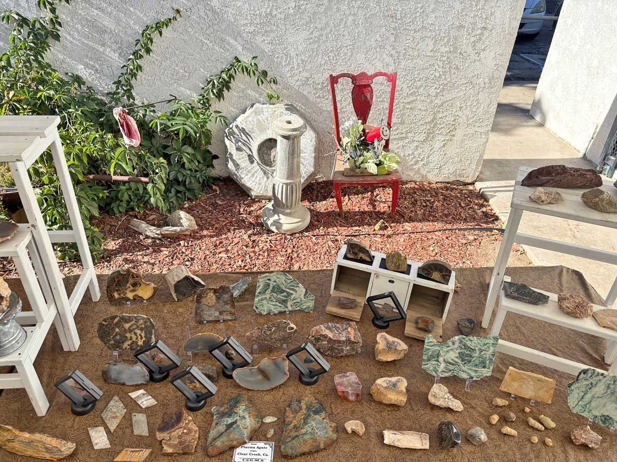 A display of various rocks and minerals set on the ground and on wooden stands in an outdoor area with a red chair.