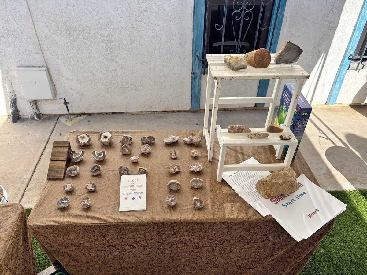 A table display of small geodes and minerals set on a burlap cloth with a small white tiered stand.