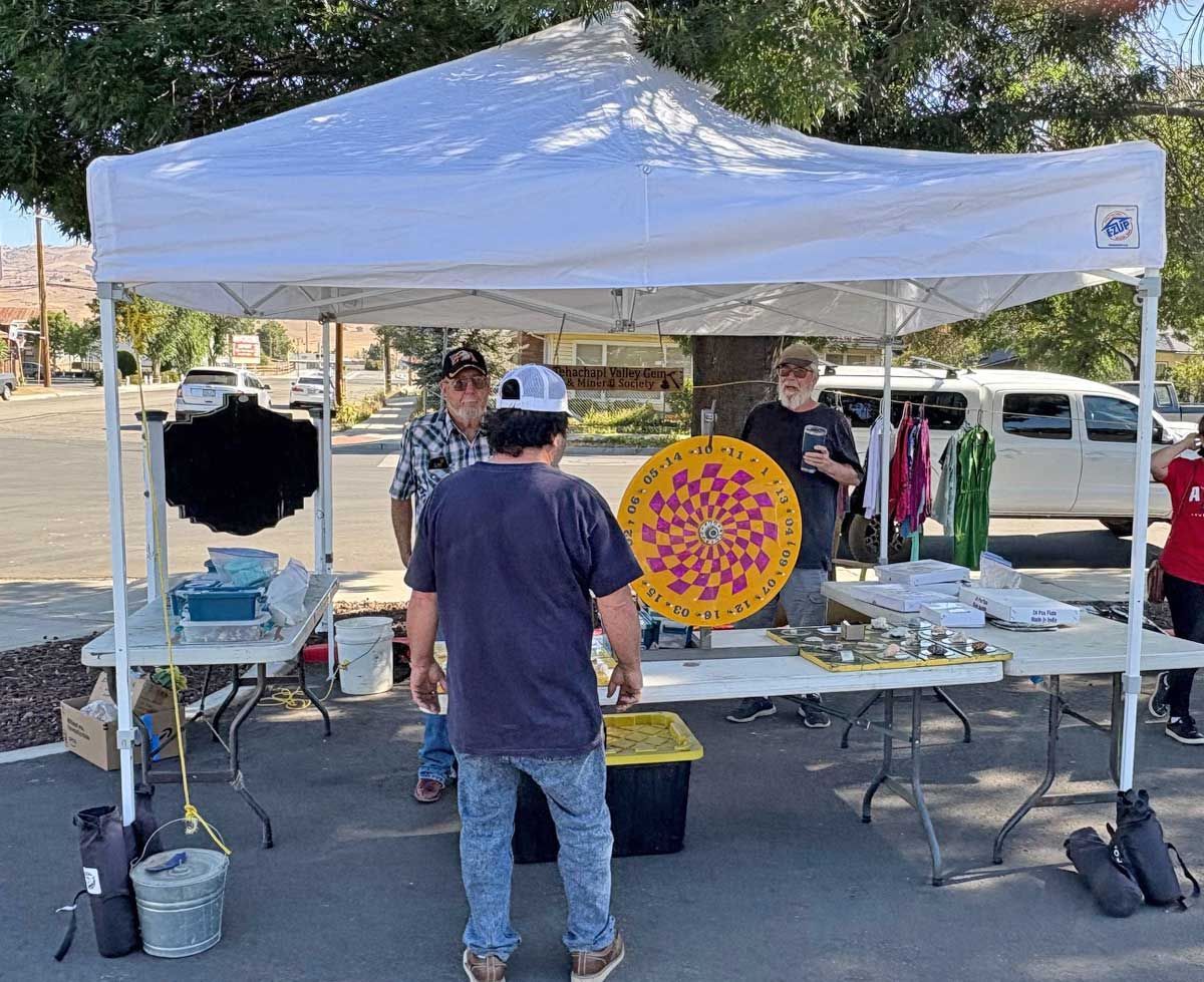 Outdoor craft booth under white canopy with colorful circular artwork on display and a person standing at the table