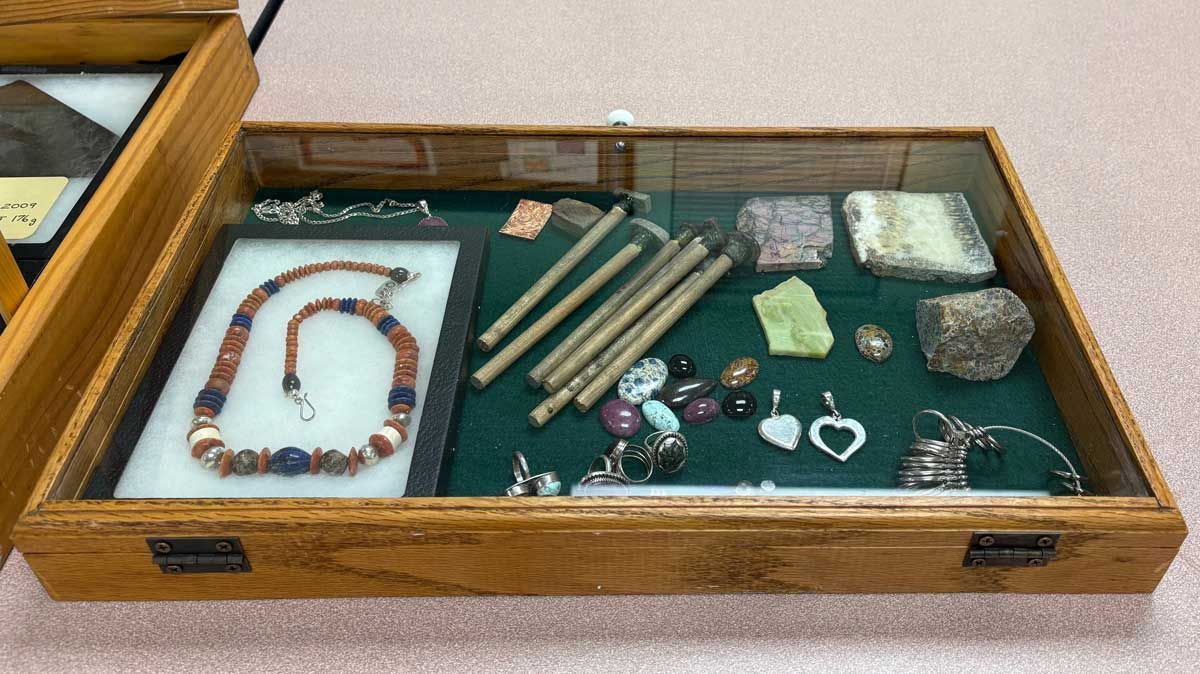 Display case of assorted jewelry, beads, crystals, and wooden rods on green felt interior.