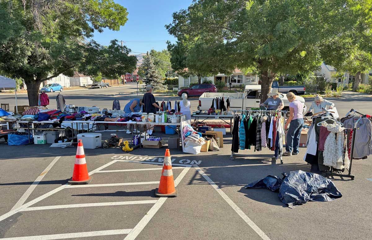 Outdoor clothing sale with tables of garments, racks of shirts, and traffic cones in a parking lot