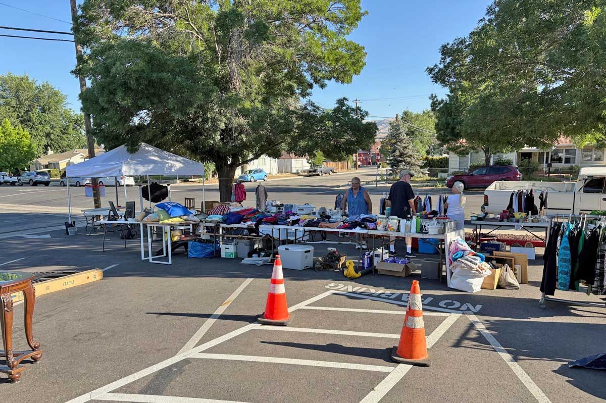 Outdoor flea market with tables of assorted goods, orange cones, and trees in a sunny parking lot