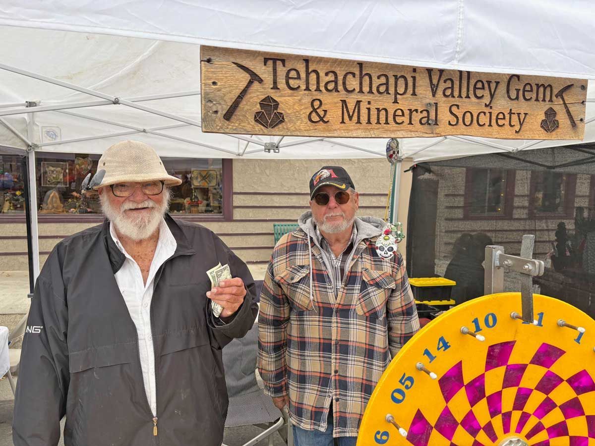 Two men standing under a Tehachapi Valley Gem & Mineral Society booth sign at an outdoor fair