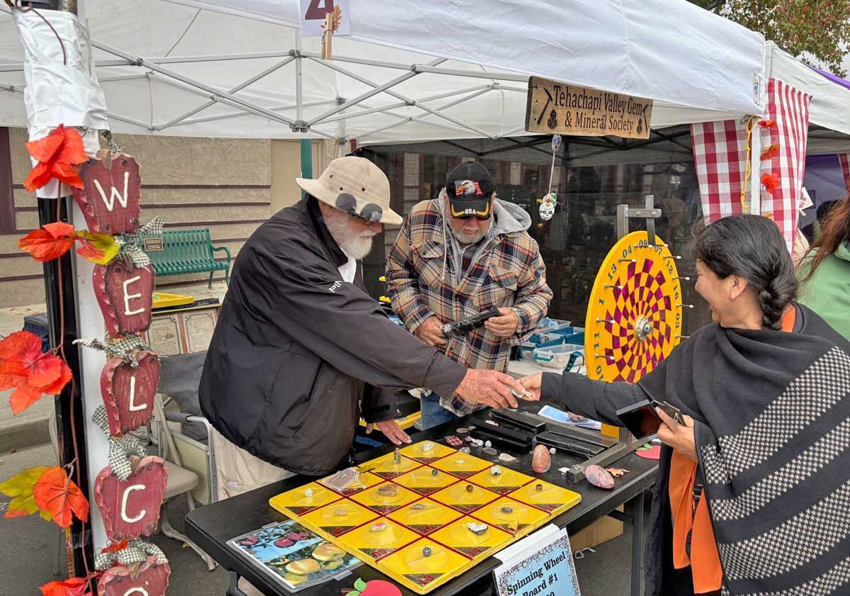 Two people at an outdoor booth exchanging items over a table of bright yellow packages