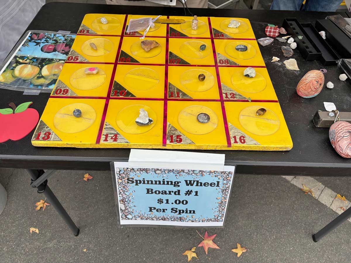 Carnival spinning wheel game with yellow numbered squares, prizes, and a sign on a table outdoors