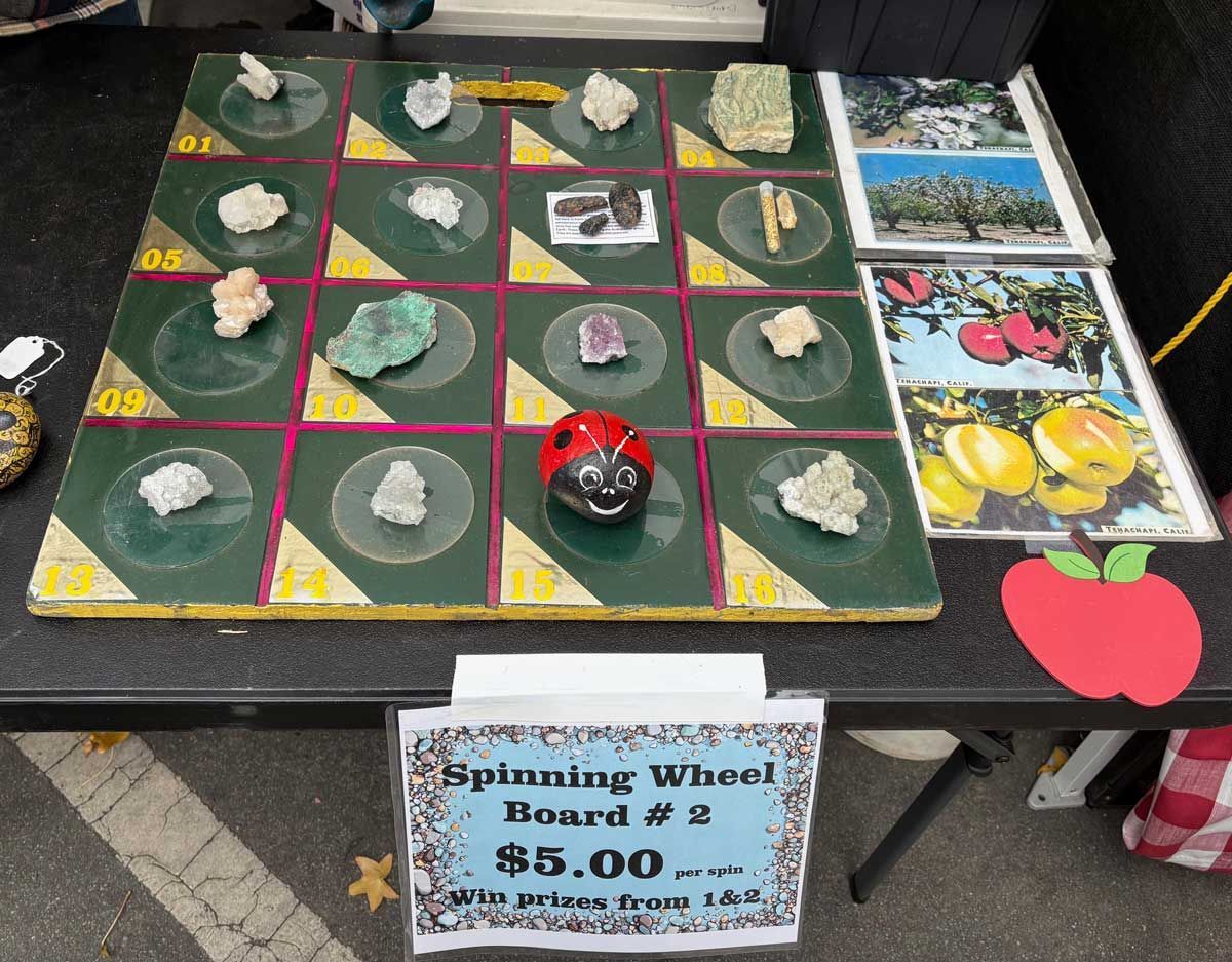 Outdoor tabletop display of small crystal stones in a grid, with a $5.00 sign and colorful gemstone photos.