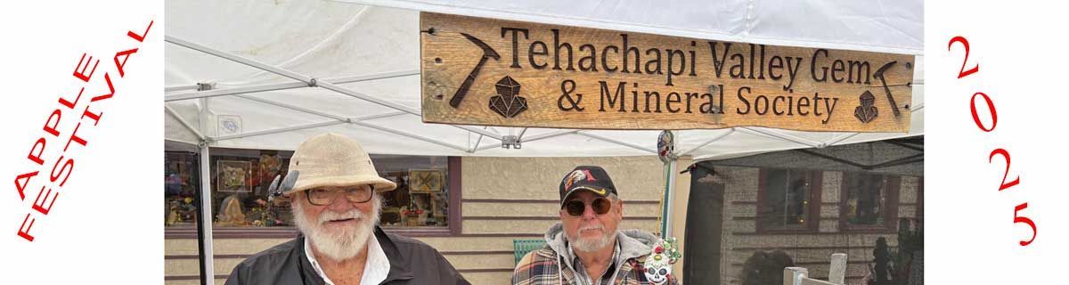 Two people standing in front of a stone building with a wooden sign reading “Tehachapi Valley Gem & Mineral Society”