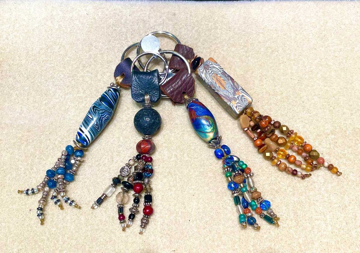 Four colorful beaded tassels hang from a circular metal ring against a neutral background.