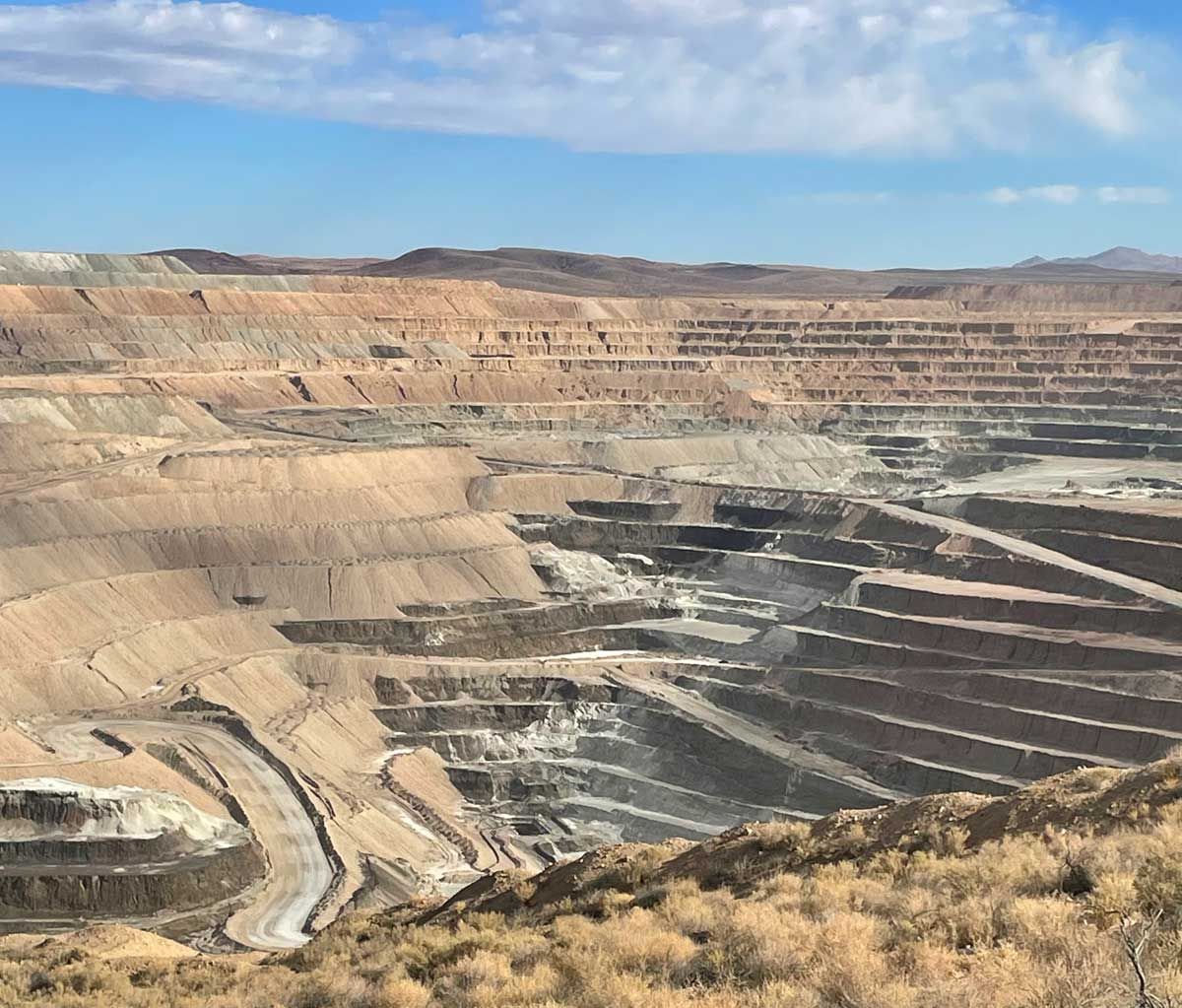 Open-pit mine with stepped terraced walls and winding haul roads in a dry desert landscape