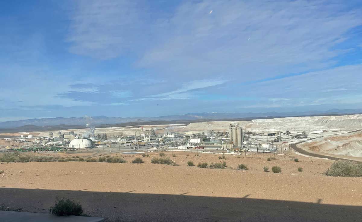 Wide cityscape with white buildings, a dirt foreground, and a blue sky over distant hills