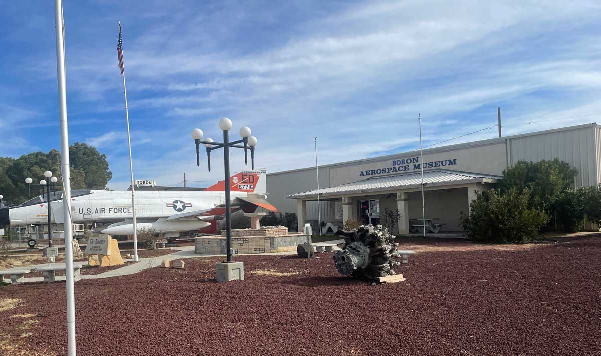 Small roadside museum with a vintage airplane exhibit and metal sculpture in front of a white building.
