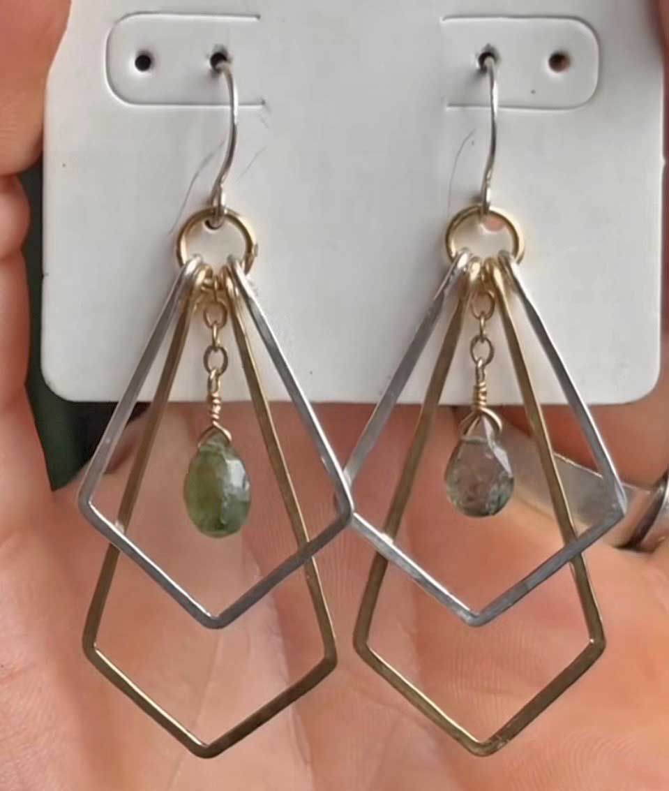 Geometric dangling earrings with green and clear stones on a display card