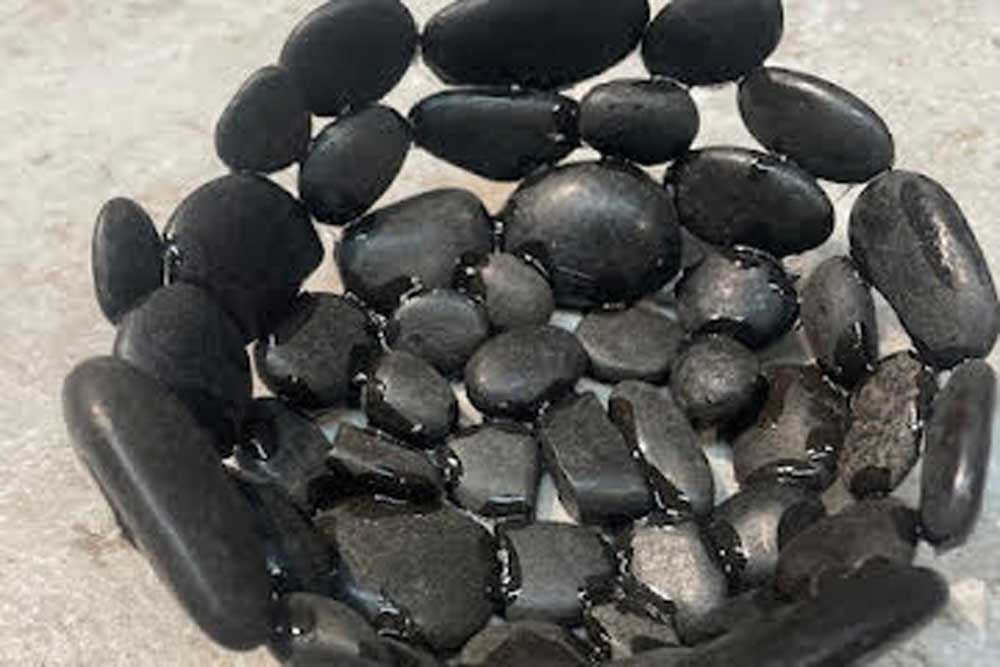A small bowl handmade from smooth, dark black river stones, resting on a textured light gray surface.