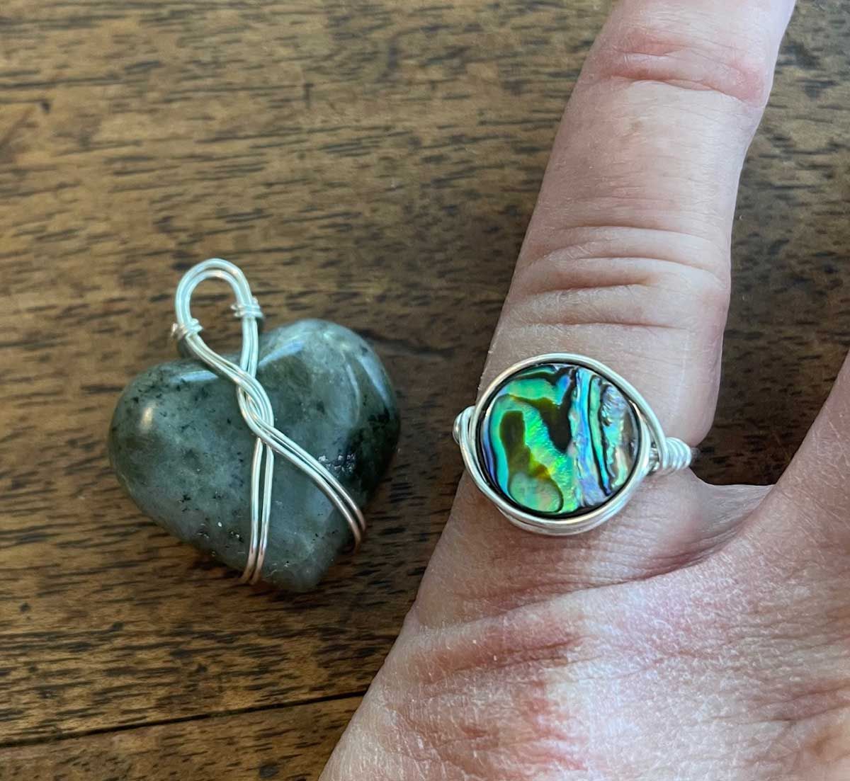 Heart-shaped stone pendant and iridescent ring on a hand over a wooden surface