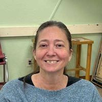 Smiling person in a blue sweater seated indoors against a light green wall.