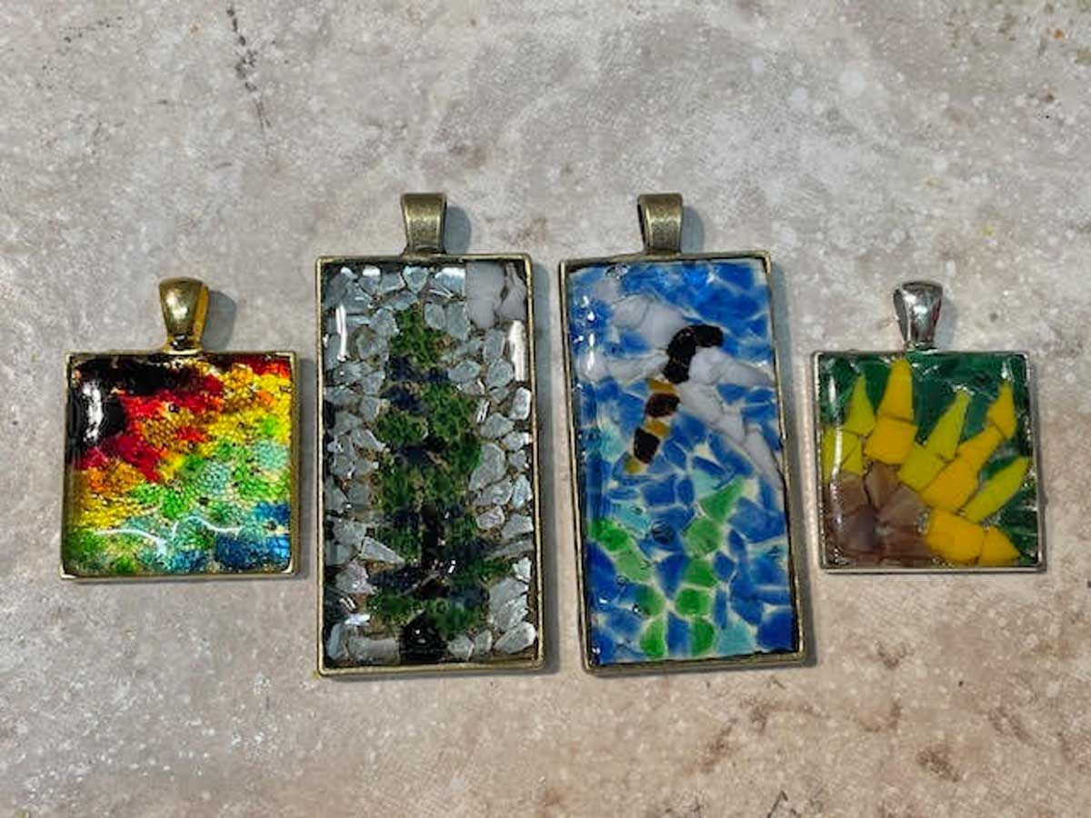 Four mosaic pendants with colorful glass designs arranged on a textured stone surface.