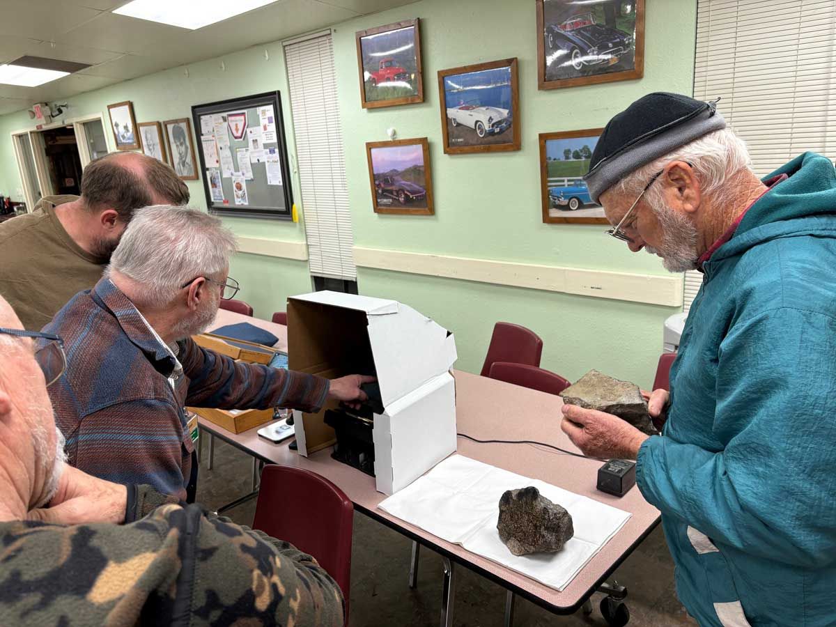 People gather around a table examining rock specimens and a portable lightbox in a room decorated with framed photos.