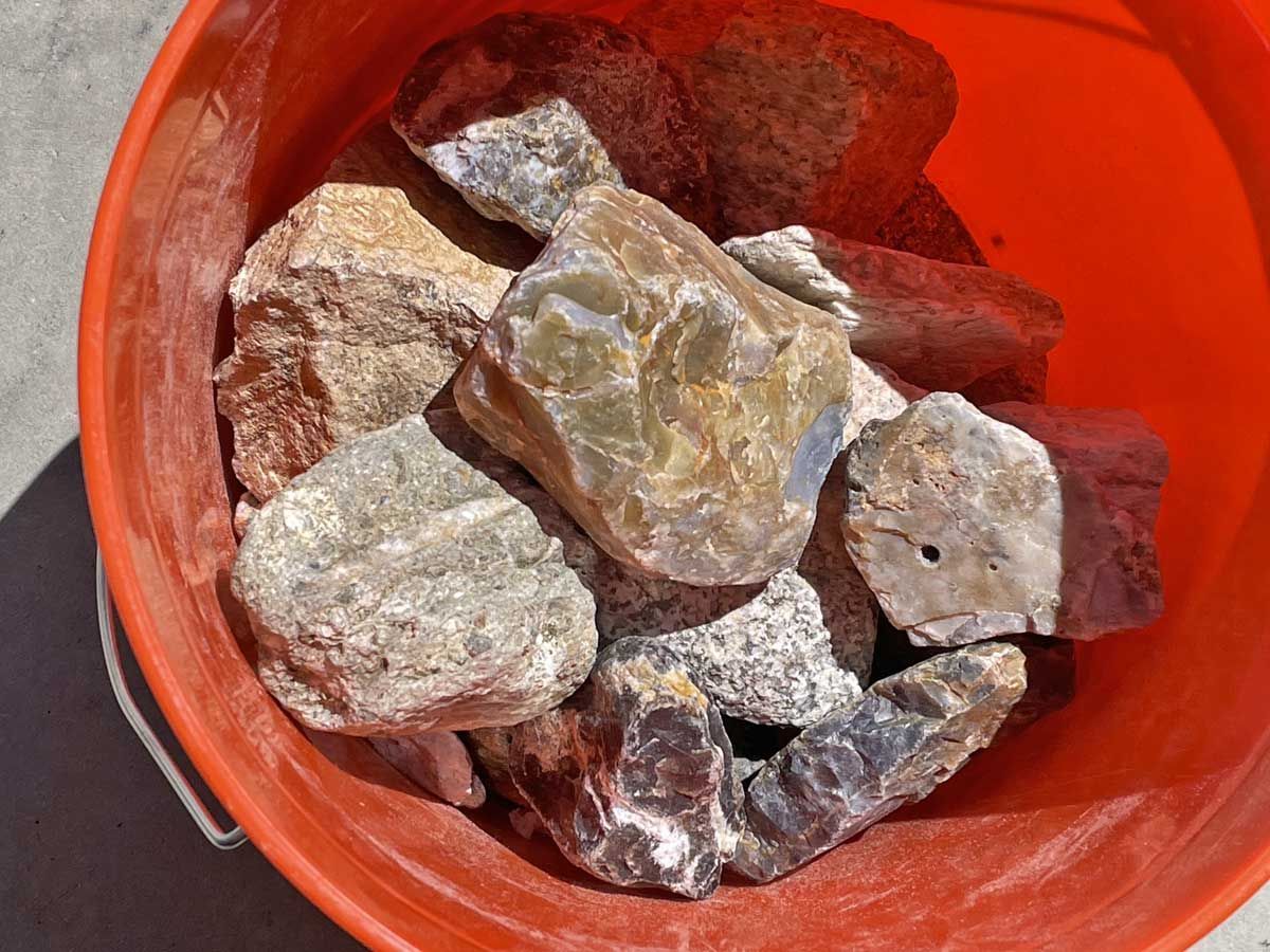 Red bucket filled with assorted rough rocks and stones