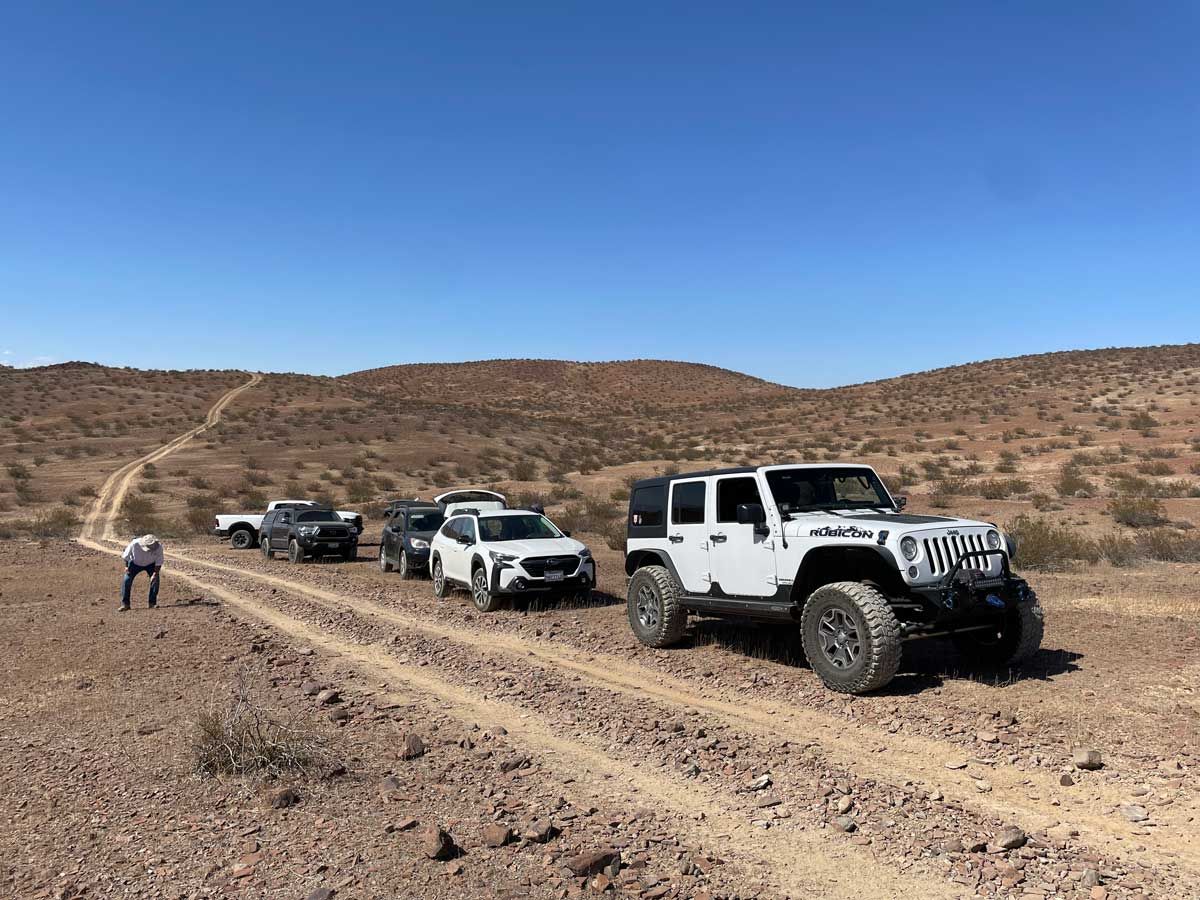 Off-road Jeep convoy on a desert trail with a person standing beside the path under a clear blue sky