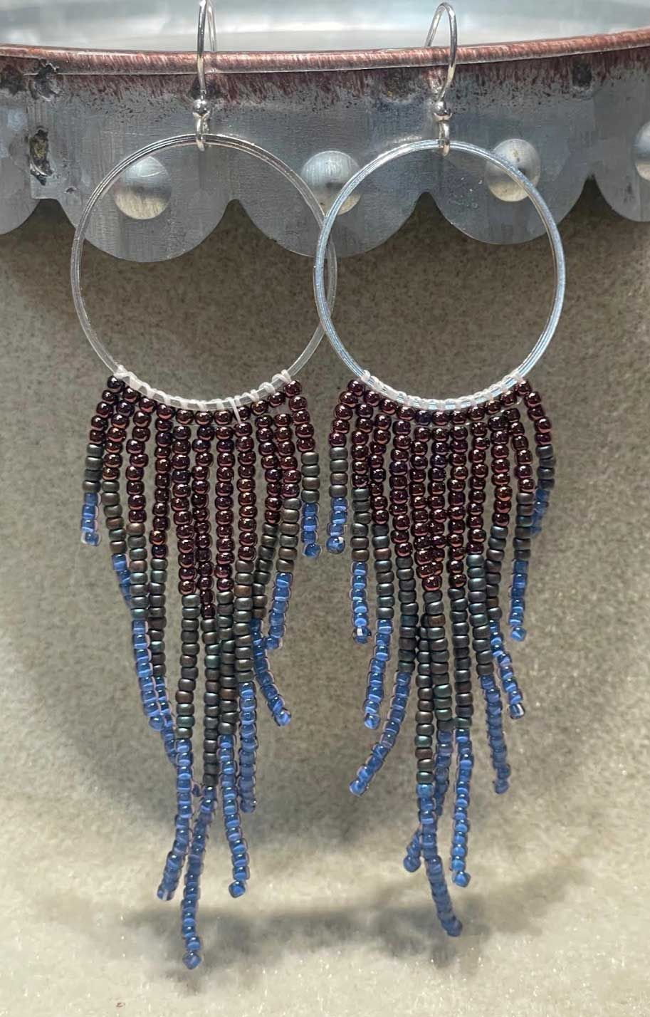 Beaded hoop earrings with dark red and blue fringes hanging from a display