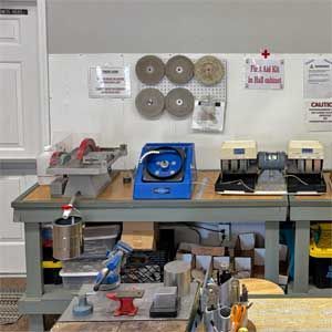 Four people stand in a workshop, smiling near shelves and boxes.