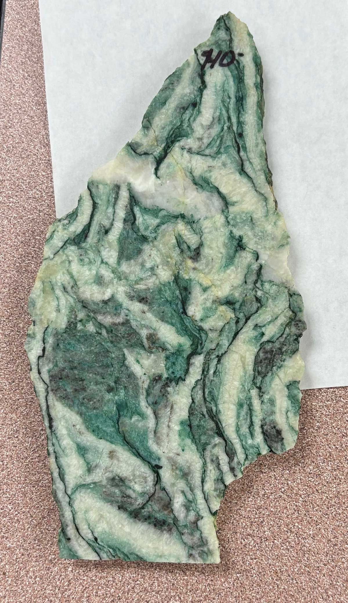 Green marbled stone fragment with irregular shape on a speckled surface