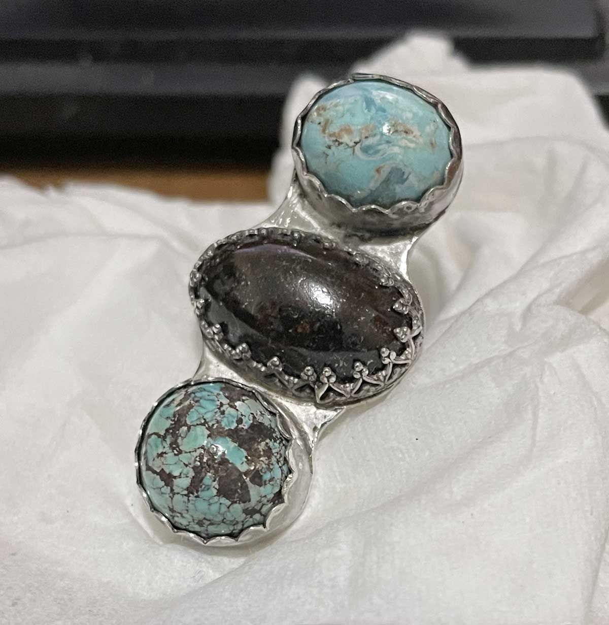 Silver ring with two turquoise stones and a dark central setting on a white tissue