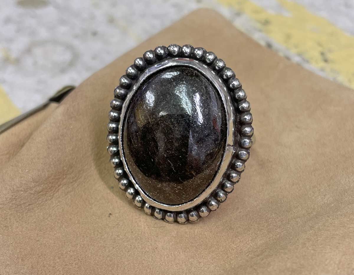 Oval dark gemstone ring with silver beaded border on tan fabric background
