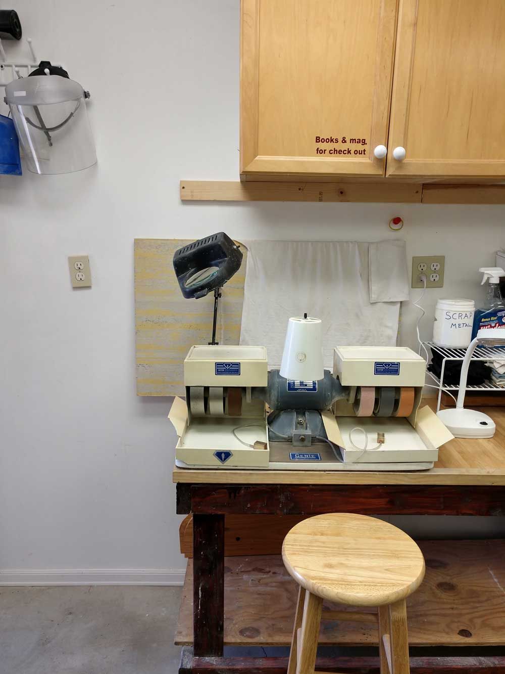 Worktable with vintage sewing machine under cabinets, with stool and task lamp in a small workshop