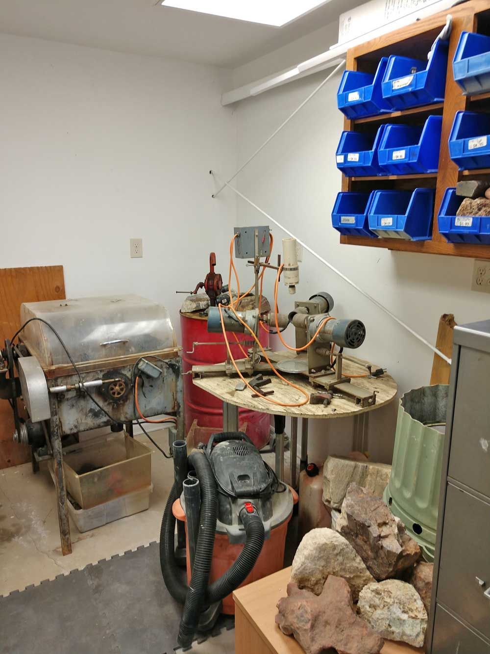 Workshop corner with metal machinery, blue bins on shelves, and tools on a workbench