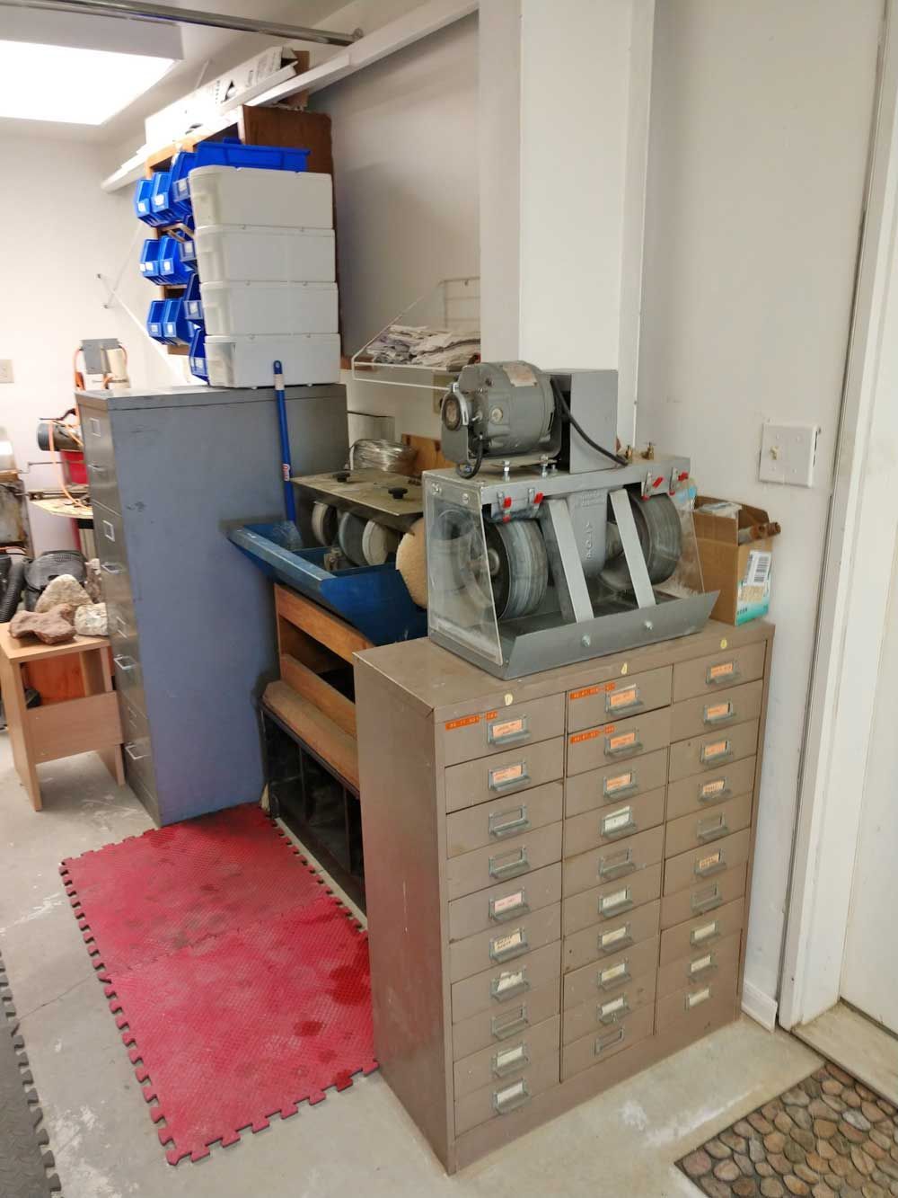 Cluttered workshop with stacked cabinets, tools, and machinery in a narrow storage area