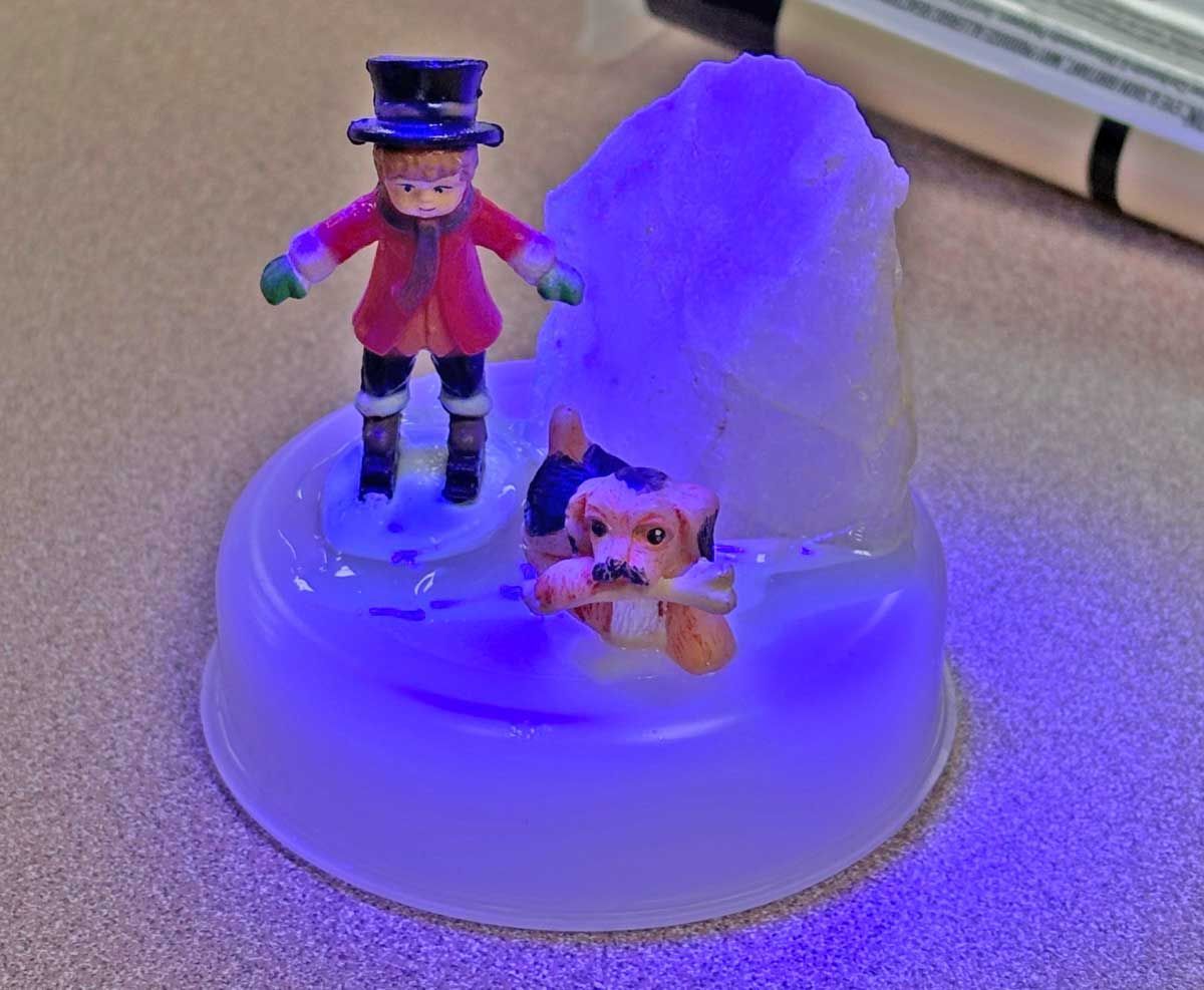 A small toy figurine of a person in a top hat and a dog with a bone, set on a plastic base illuminated by purple light.