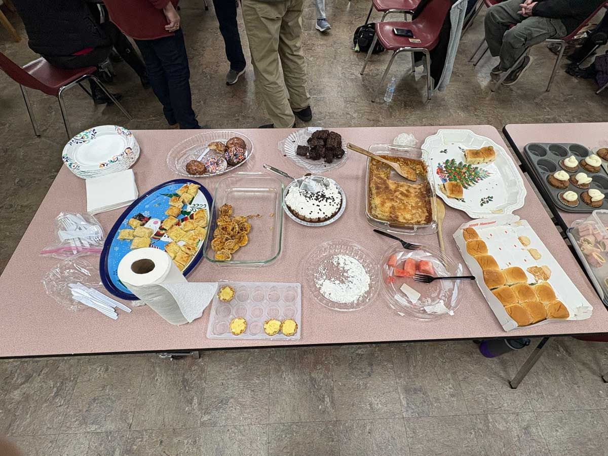 A table covered in various food dishes including a tray of rolls, a casserole, cookies, and paper goods.