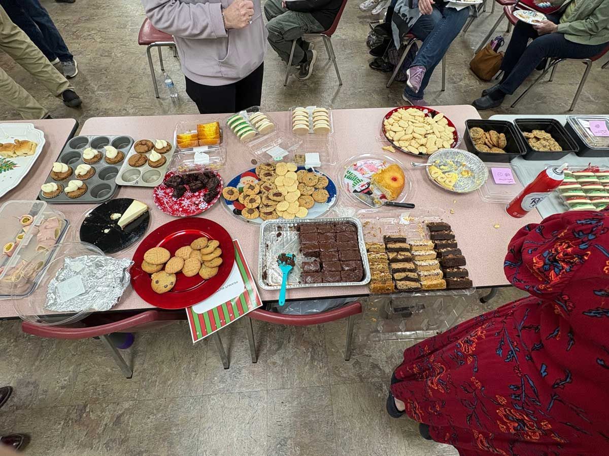 A large table spread featuring various holiday cookies, brownies, and treats at an indoor social gathering.