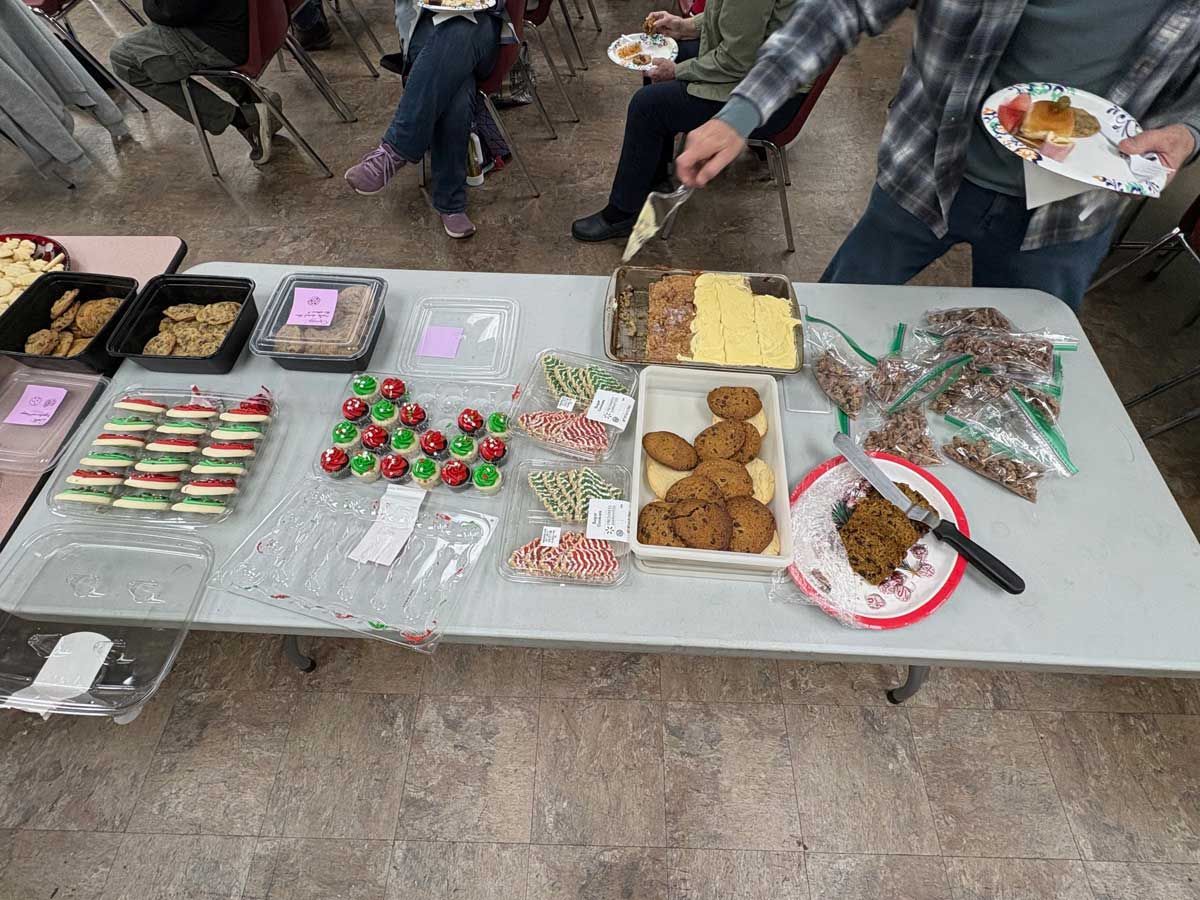 People serve themselves food from a table filled with various cookies and treats at a gathering.