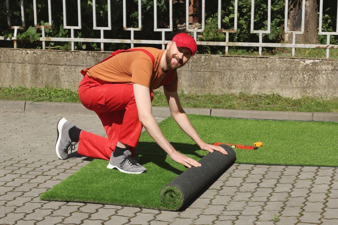 Person in orange and red rolling up a strip of artificial turf outdoors.