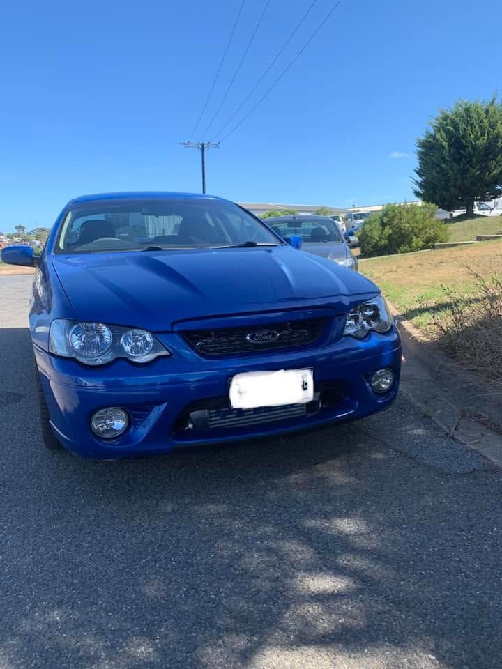 Blue sports sedan parked on a roadside under a clear blue sky