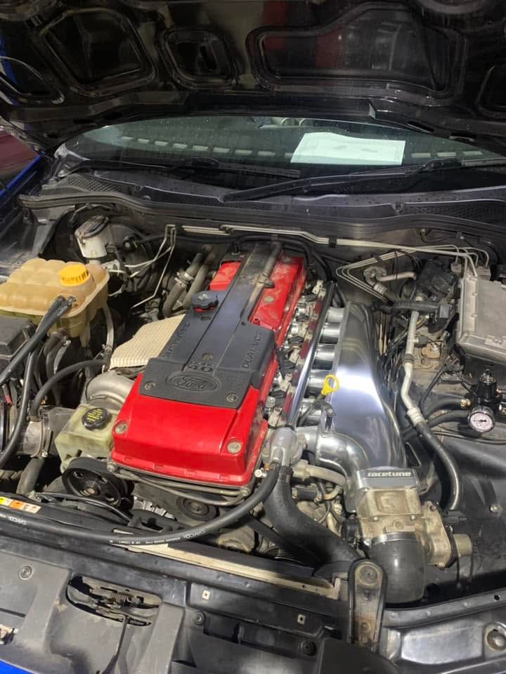 Car engine bay with red valve cover, chrome intake, and hood open, showing mechanical components.