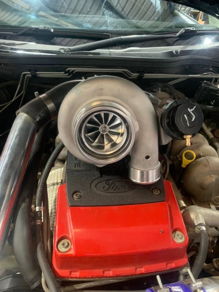 Close-up of a turbocharged car engine with red valve cover and silver turbo compressor in the engine bay