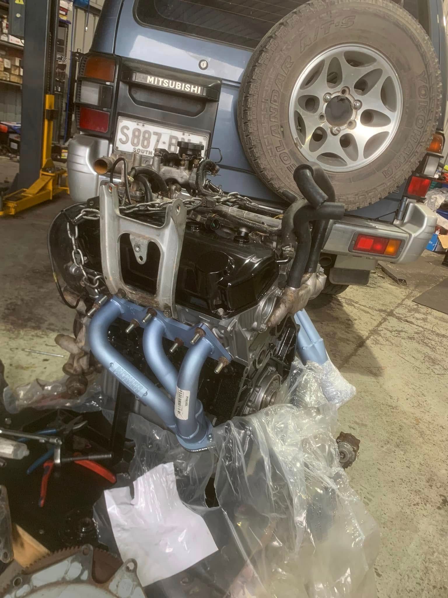 Truck under repair with exposed engine, spare tire, and tools in a garage