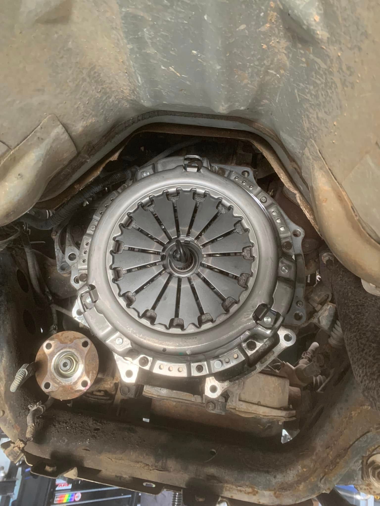Car engine clutch assembly exposed inside the transmission bell housing, with metal components and grime.