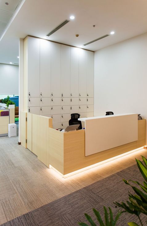 Modern office reception desk with light wood paneling, white walls, and warm floor lighting