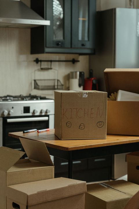 Cardboard boxes stacked in a kitchen with a stove, cabinets, and a table.