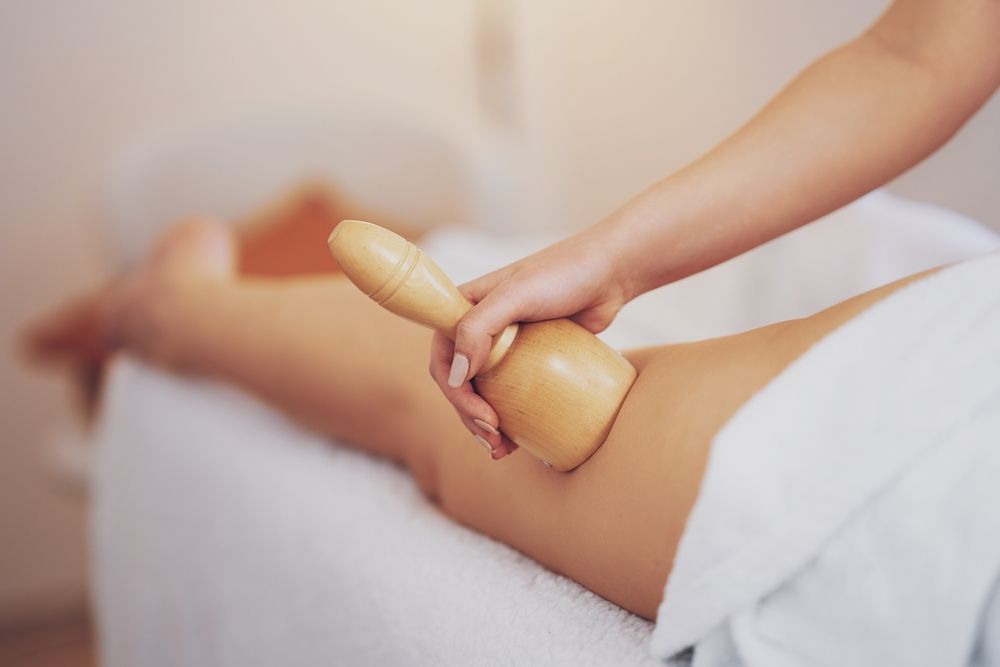 Person receiving wooden massage tool during Maderotherapy therapy on their leg.