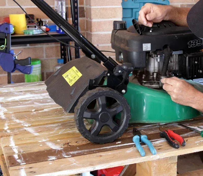 Man In Cap Repairs A Green Lawnmower On A Wooden Pallet — Jack Too You Mobile Servicing and Repairs In Sunshine Coast, QLD