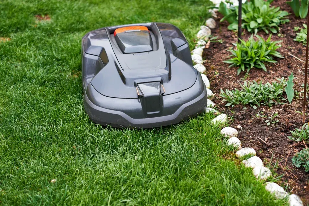 Robotic lawnmower on green grass, near a flower bed with white stones — Jack Too You Mobile Servicing and Repairs In Goomboorian, QLD