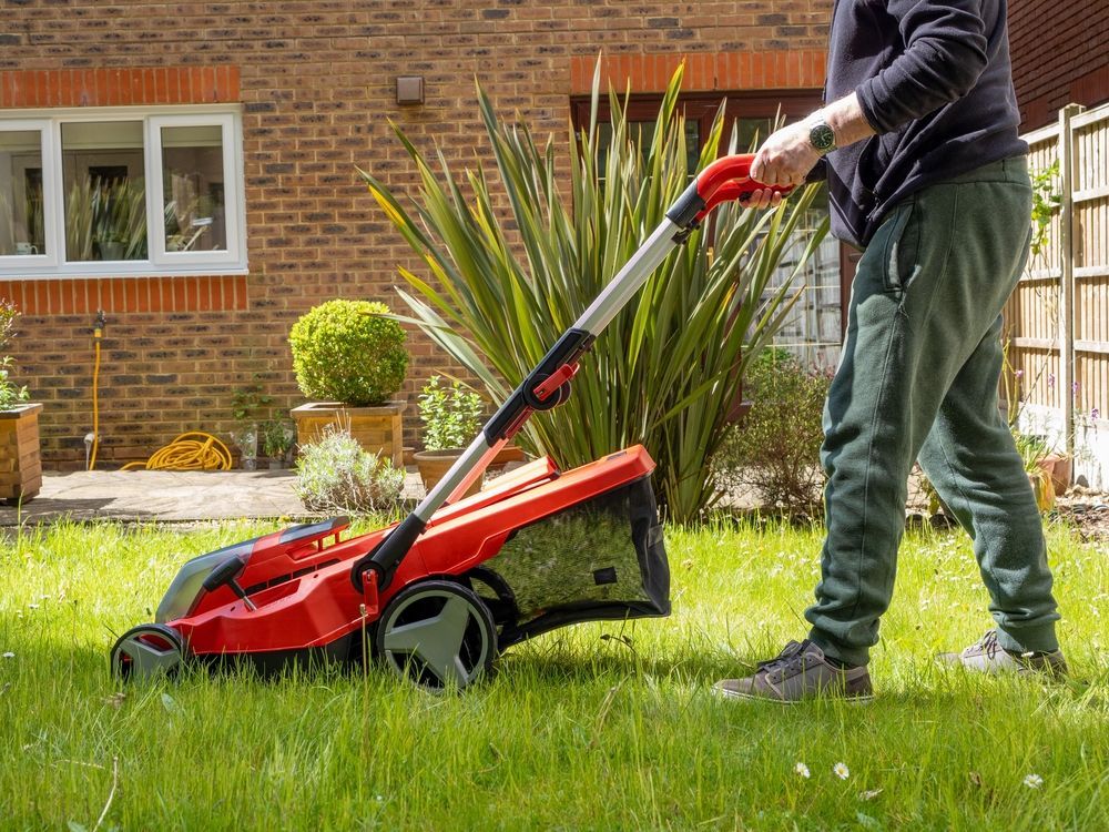 Person mowing a lawn with a red electric mower in a yard next to a brick house — Jack Too You Mobile Servicing and Repairs In Yandina, QLD