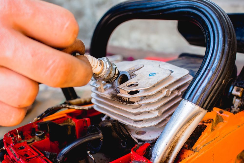 A Hand Installing A Spark Plug In A Chainsaw Engine — Jack Too You Mobile Servicing and Repairs In Goomboorian, QLD