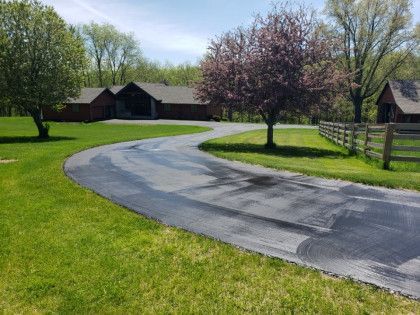 A curvy driveway leading to a large house with a fence and trees.