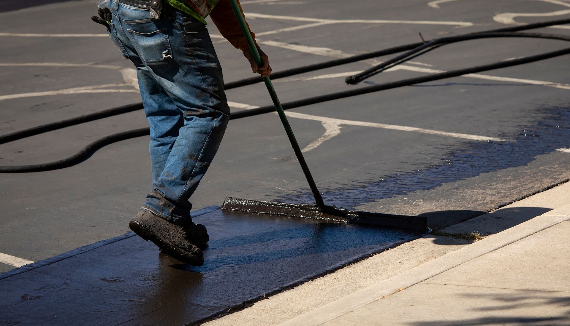 A man is spreading asphalt on the ground with a broom.